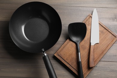 Black metal wok, knife, board and spatula on wooden table, top view