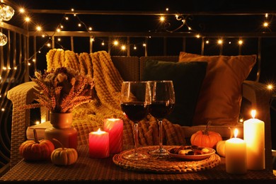 Glasses of wine, burning candles and autumn decor on outdoor terrace in evening