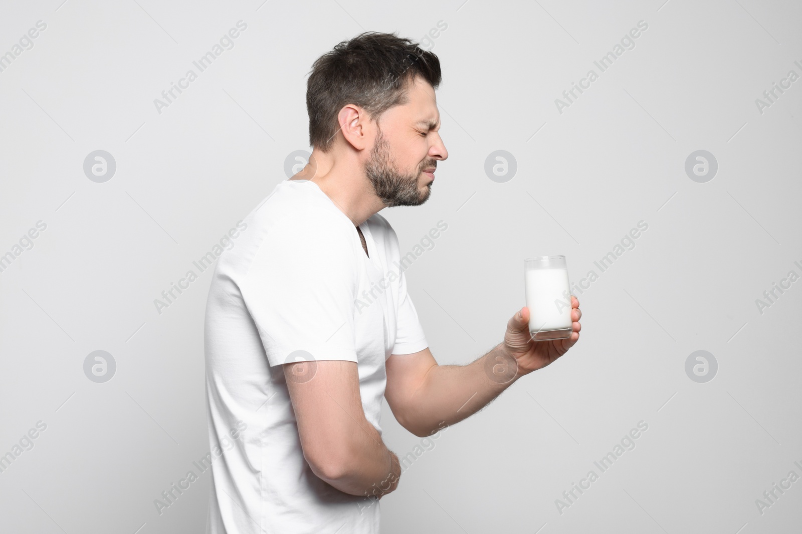 Photo of Man with glass of milk suffering from lactose intolerance on white background