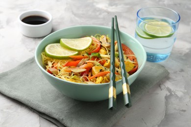 Photo of Stir-fry. Delicious cooked noodles with chicken and vegetables in bowl served on gray textured table