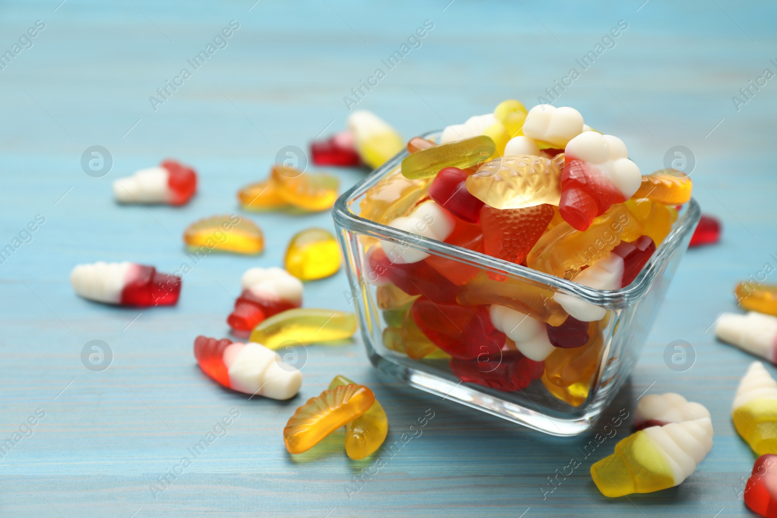 Photo of Many different delicious gummy candies on light blue wooden table, closeup. Space for text