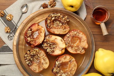 Tasty baked quinces with walnuts and honey in bowl on wooden table, flat lay