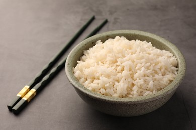 Photo of Delicious rice in bowl and chopsticks on grey table