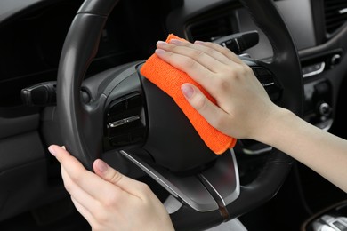 Photo of Woman cleaning steering wheel with rag in car, closeup