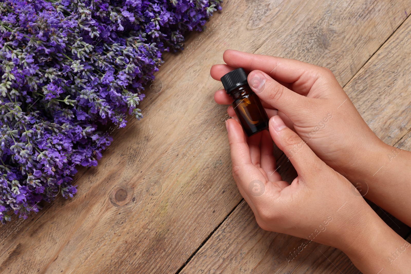 Photo of Woman with bottle of lavender essential oil and flowers on wooden background, top view