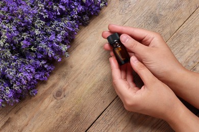 Photo of Woman with bottle of lavender essential oil and flowers on wooden background, top view