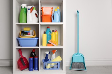 Photo of Shelving unit with detergents and cleaning tools near white wall indoors