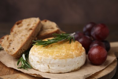 Photo of Tasty baked camembert, pieces of bread, grapes and rosemary on table, closeup