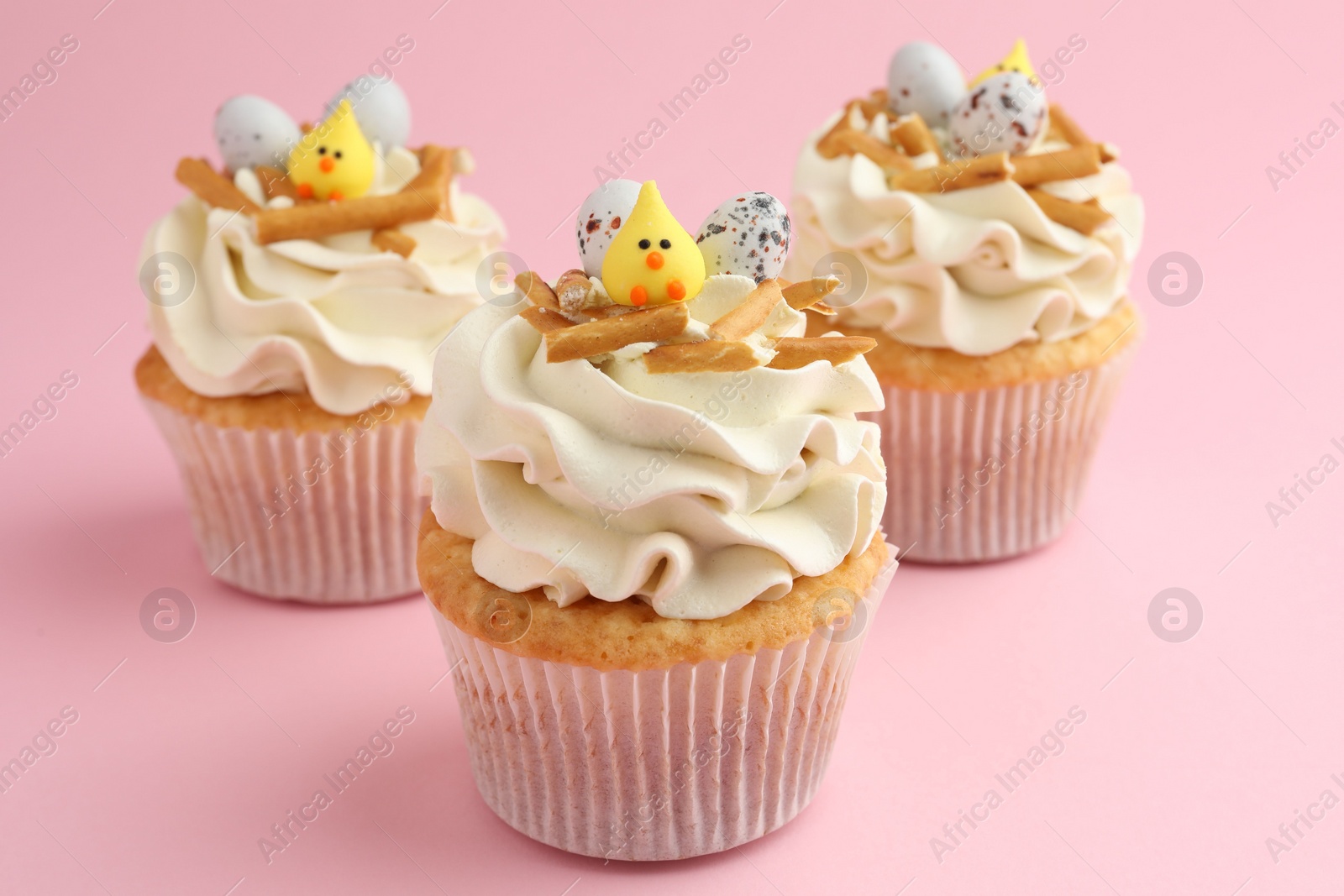 Photo of Tasty Easter cupcakes with vanilla cream on pink background, closeup