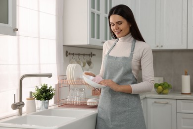 Photo of Happy woman wiping bowl with towel in kitchen, space for text