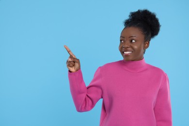 Happy young woman pointing at something on light blue background. Space for text