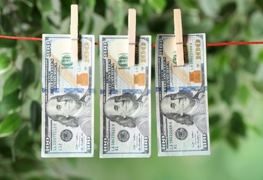 Photo of Dollar banknotes hanging on rope against blurred green background