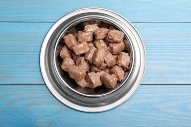 Wet pet food in feeding bowl on light blue wooden table, top view