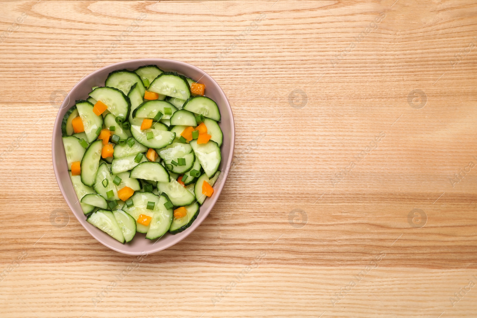 Photo of Tasty fresh salad with cucumber in bowl on wooden table, top view. Space for text