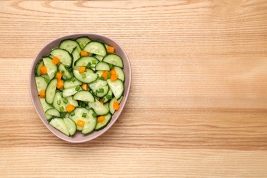 Photo of Tasty fresh salad with cucumber in bowl on wooden table, top view. Space for text