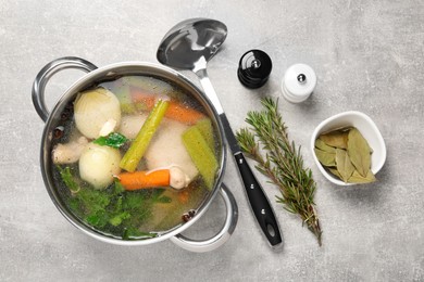 Pot with tasty bouillon and different ingredients on light grey table, flat lay