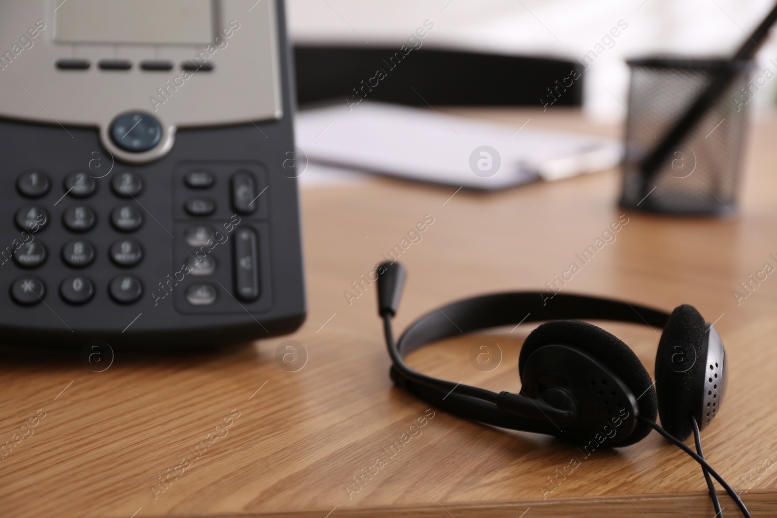 Photo of Office desktop telephone and headset on wooden table, closeup. Hotline service