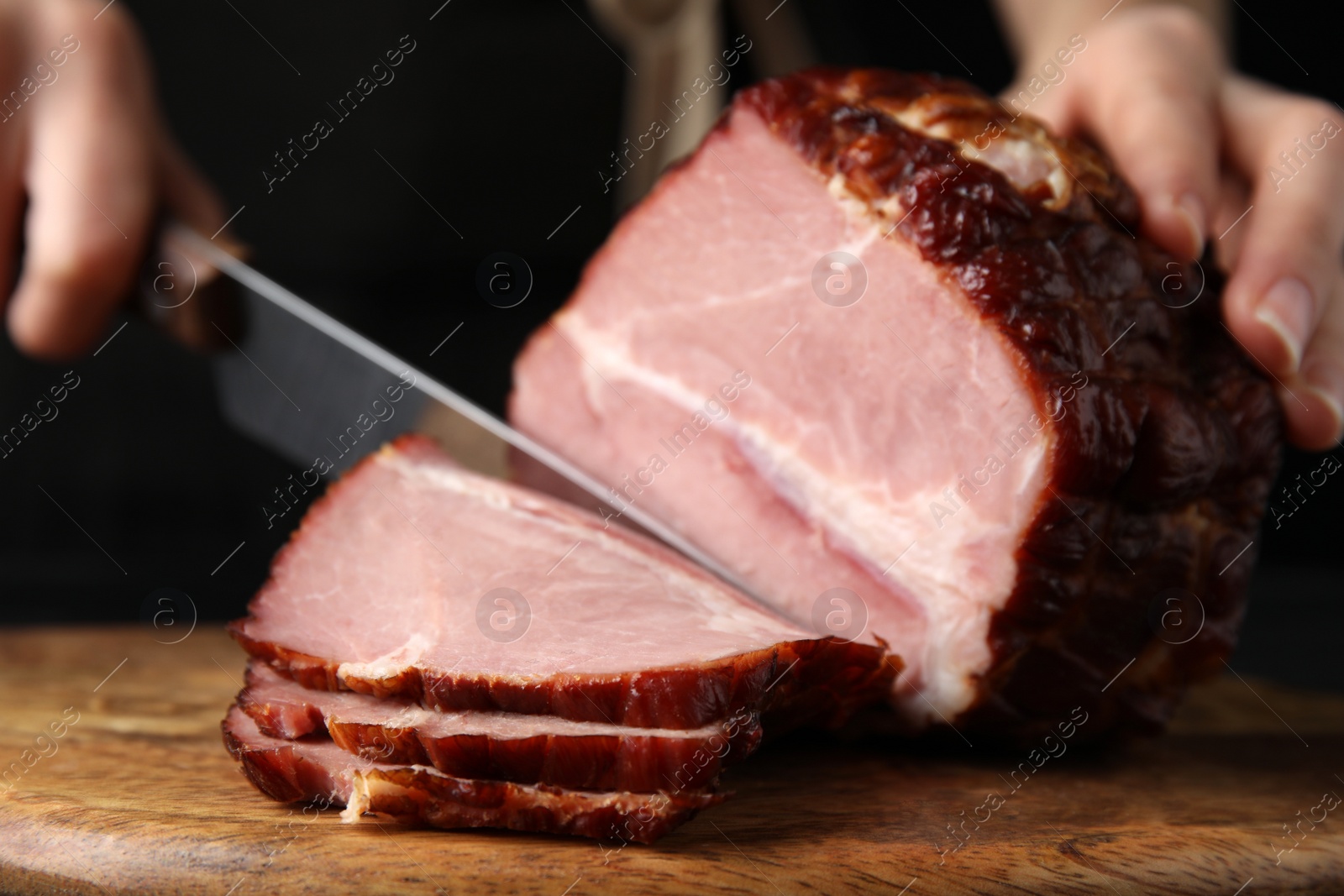 Photo of Woman cutting ham on wooden board, closeup