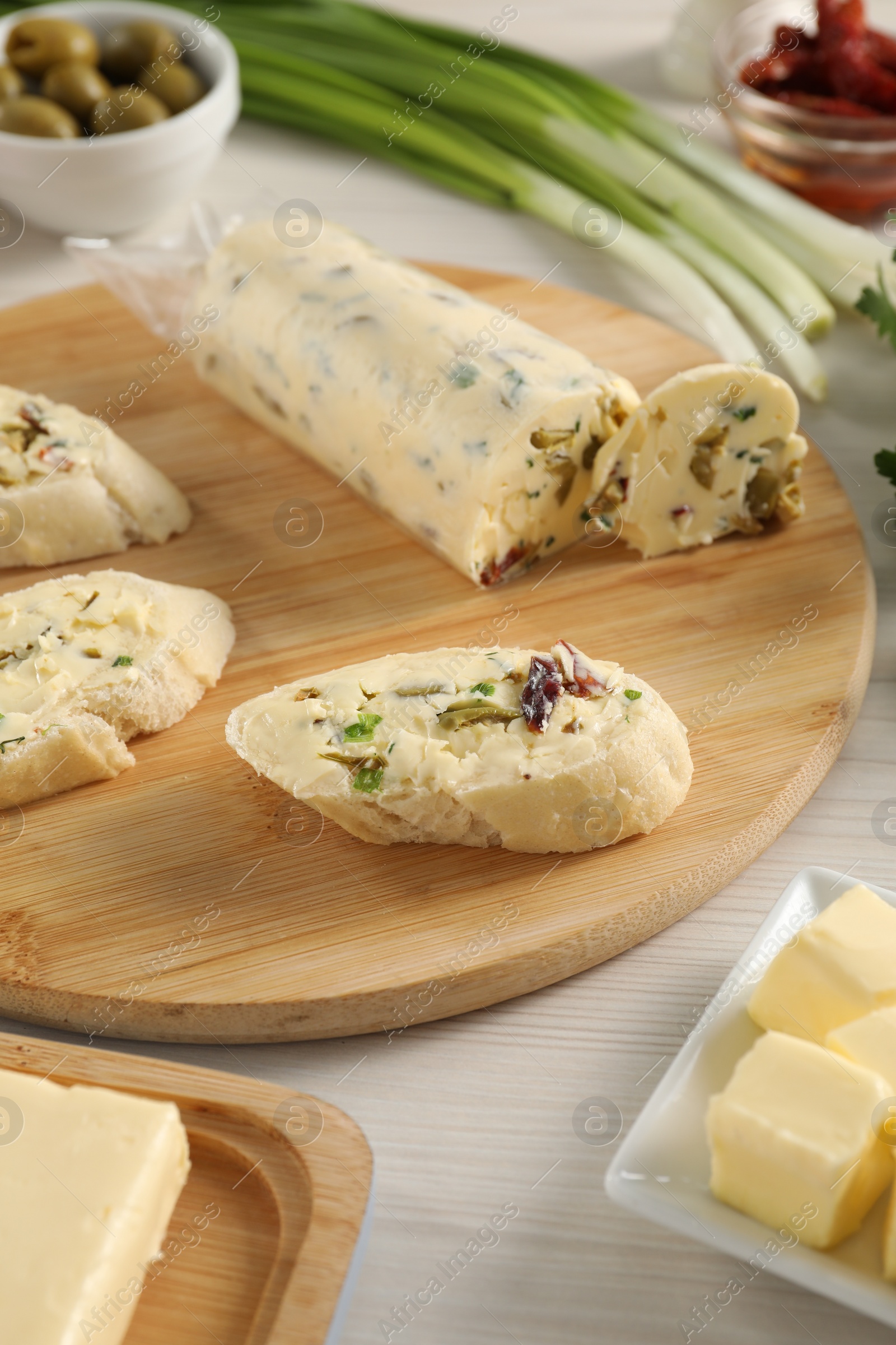 Photo of Tasty butter with olives, green onion and bread on wooden table