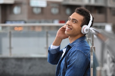 Handsome young African-American man with headphones listening to music on city street. Space for text