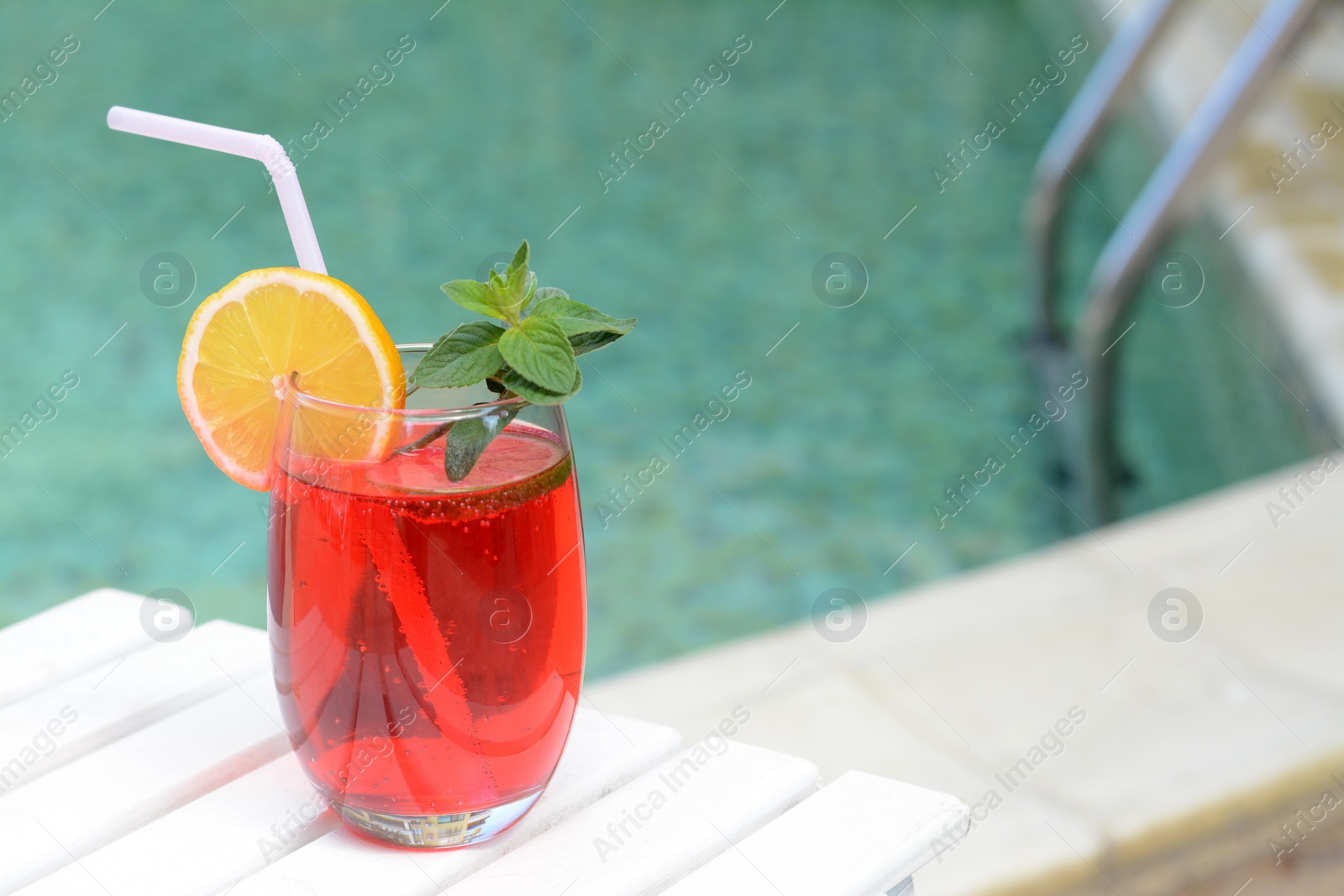 Photo of Glass of delicious cocktail on white wooden table near swimming pool, space for text. Refreshing drink