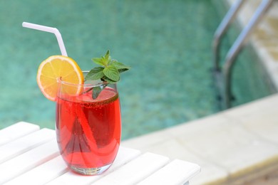 Glass of delicious cocktail on white wooden table near swimming pool, space for text. Refreshing drink