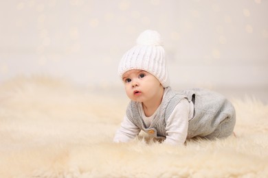 Photo of Cute baby on fluffy carpet against blurred festive lights, space for text. Winter holiday