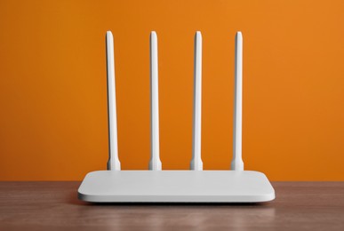Photo of New modern Wi-Fi router on wooden table near orange wall