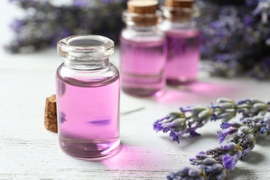 Bottles with essential oil and lavender flowers on white wooden table