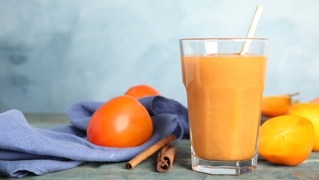 Photo of Tasty persimmon smoothie with straw on wooden table against light blue background. Space for text