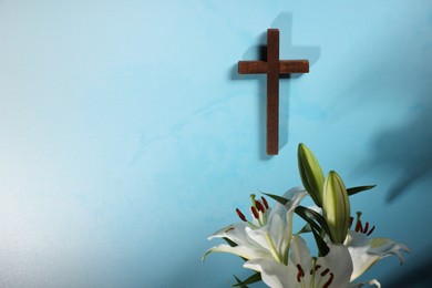 Wooden cross and lily flowers on light blue background, space for text. Religion of Christianity