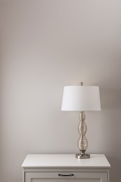 Photo of Wooden nightstand with lamp near white wall in room
