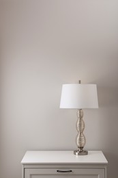 Wooden nightstand with lamp near white wall in room