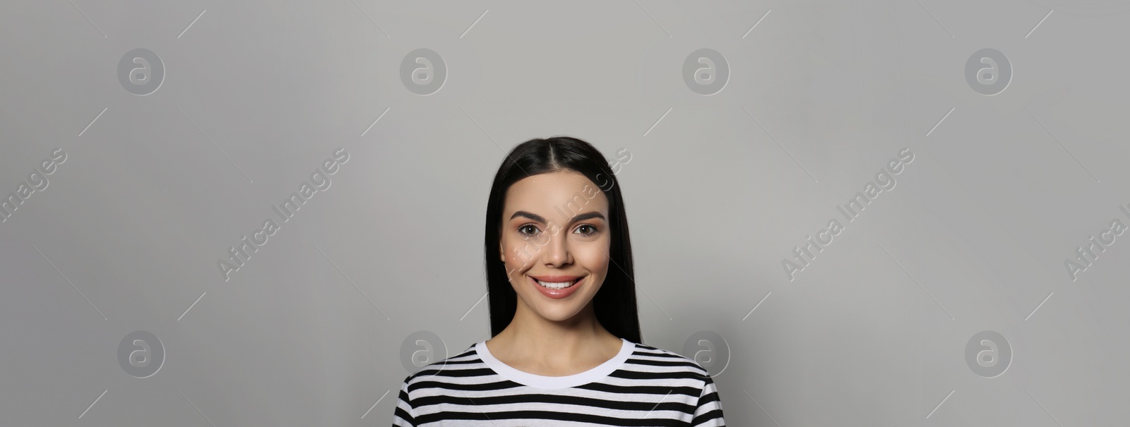 Image of Portrait of happy young woman with beautiful black hair and charming smile on light grey background. Horizontal banner design