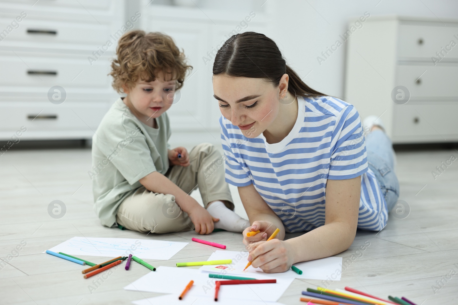 Photo of Mother and her little son drawing with colorful markers on floor at home