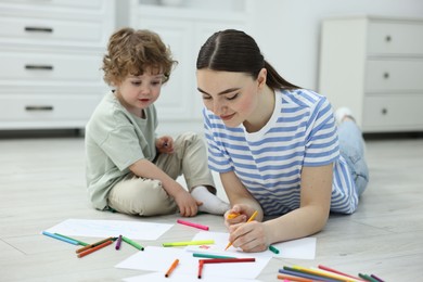 Mother and her little son drawing with colorful markers on floor at home