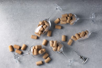 Glasses with many wine corks and corkscrew on light grey table, flat lay