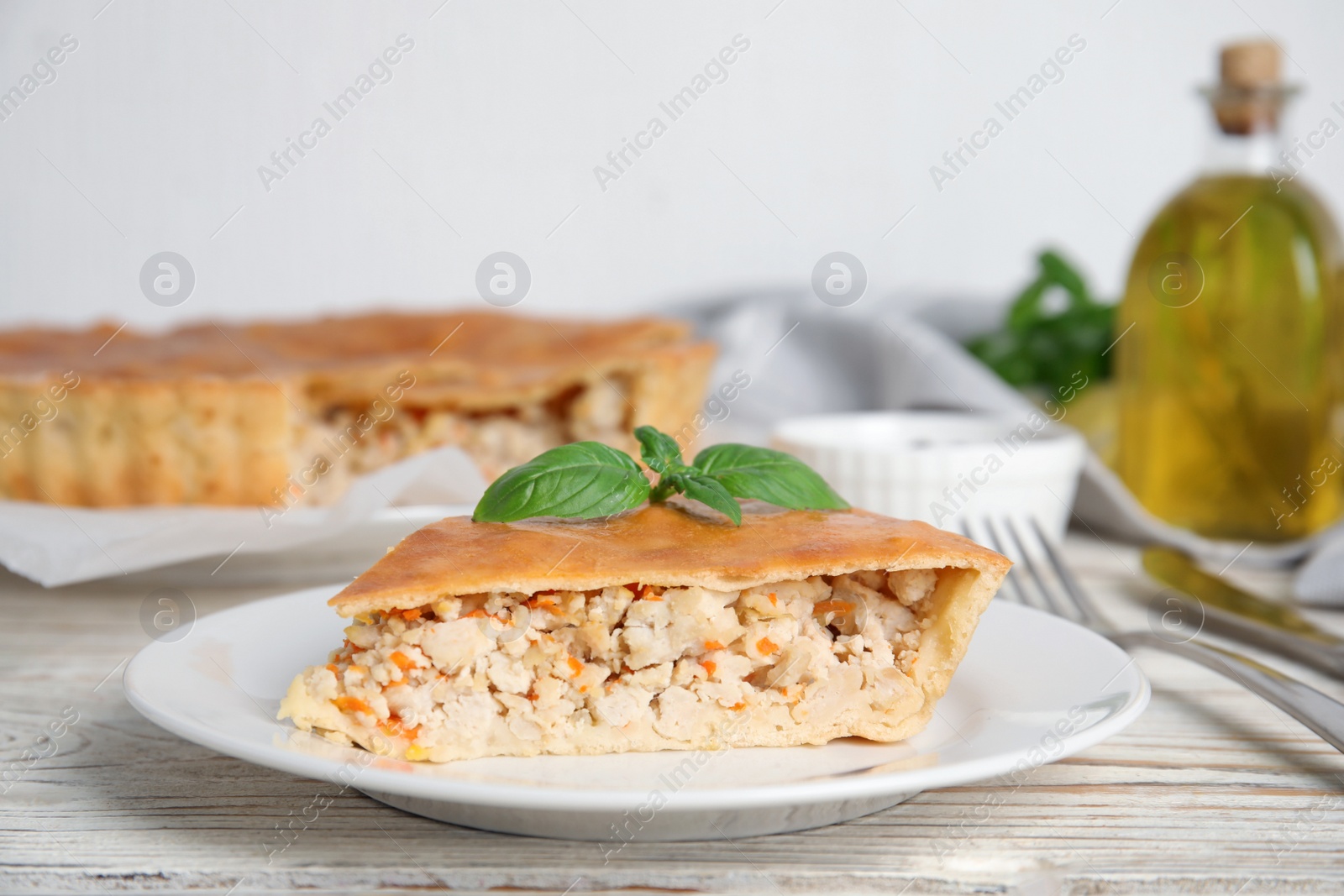 Photo of Slice of delicious meat pie with basil on white wooden table, space for text