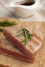 Photo of Pieces of delicious tuna with rosemary on parchment paper, closeup
