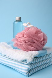 Pink shower puff, bottle of cosmetic product and towel on light blue background, closeup