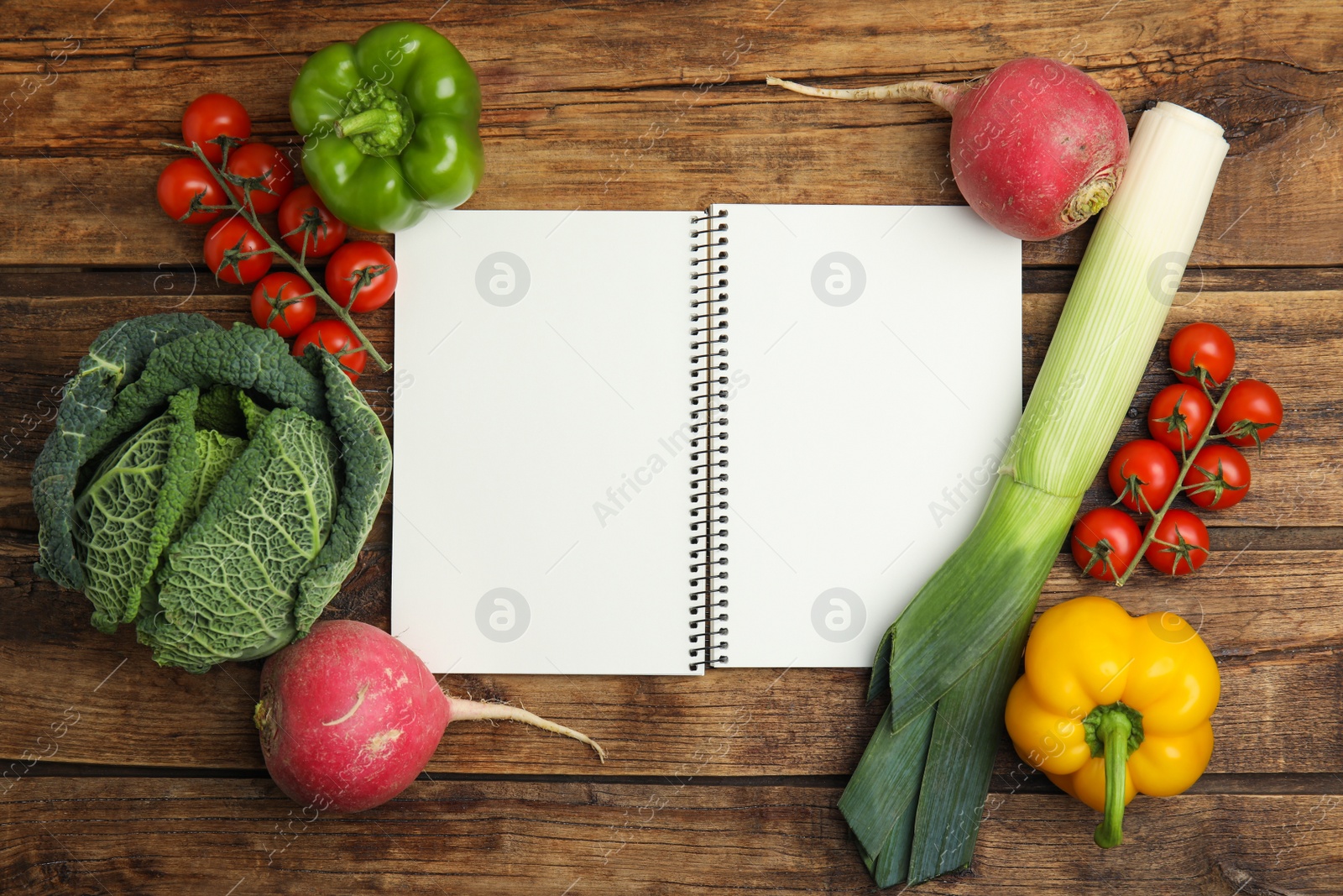 Photo of Recipe book surrounded by different fresh vegetables on wooden table, flat lay with space for text. Cooking classes