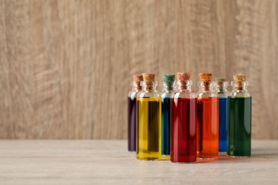 Photo of Glass bottles with different food coloring on wooden table. Space for text