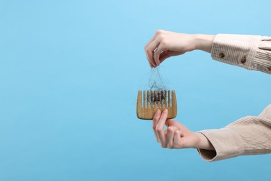 Photo of Woman untangling her lost hair from comb on light blue background, closeup and space for text. Alopecia problem