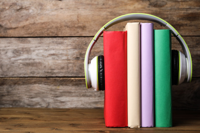 Photo of Books and modern headphones on wooden table. Space for text