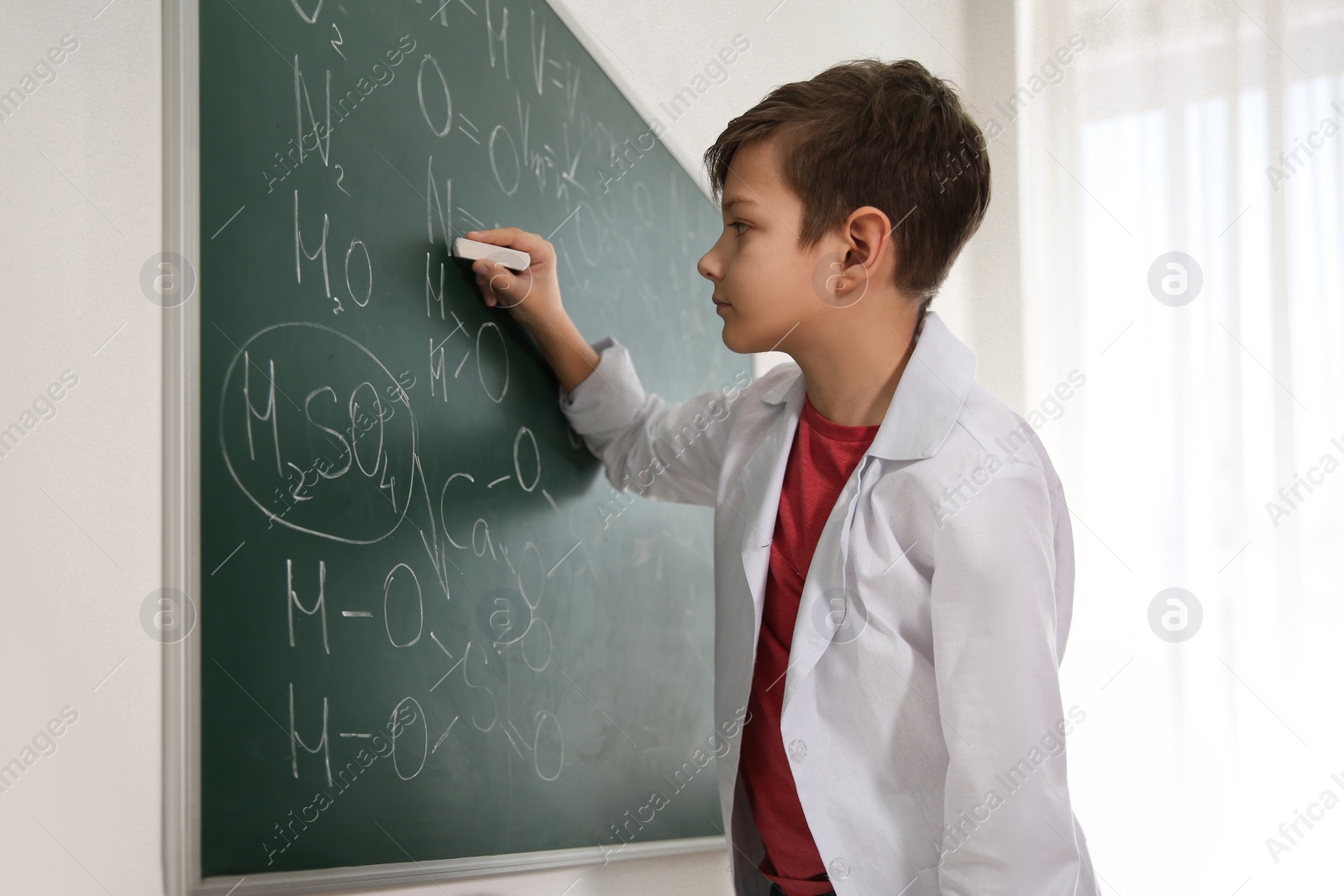 Photo of Schoolboy writing chemical formulas on chalkboard in classroom