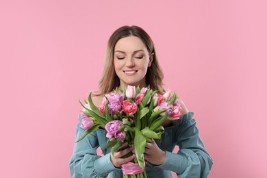 Happy young woman with bouquet of beautiful tulips on pink background