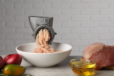 Metal meat grinder with chicken mince and different products on light grey table