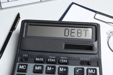 Calculator with word Debt on white table, closeup