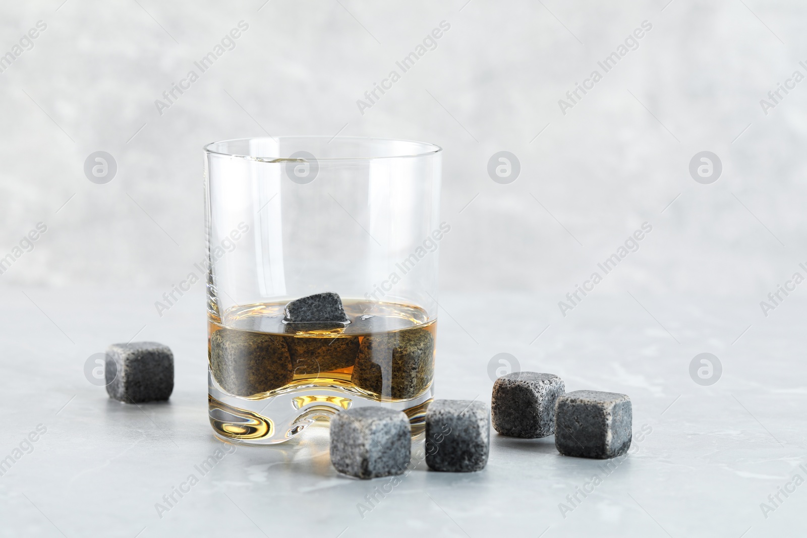 Photo of Whiskey stones and drink in glass on light marble table, closeup. Space for text