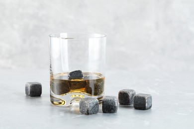 Whiskey stones and drink in glass on light marble table, closeup. Space for text